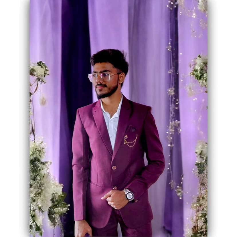 Umer Saiyad, Full Stack Developer from Surat, wearing a purple formal suit, a white dress shirt, and clear glasses, posing against a purple draped background with floral arrangements.